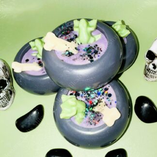 Halloween wax melts shaped like black cauldrons filled with purple wax, decorated with glitter with bones and toads